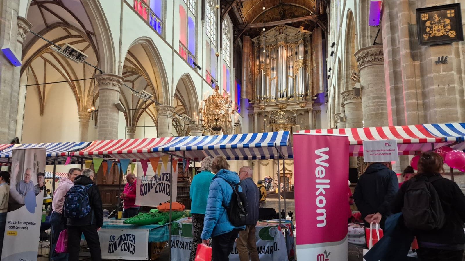 Interieur Grote Kerk met rood-wit gestreepte markttentenhuizen, bezoekers lopen tussen kramen, orgel zichtbaar op achtergrond