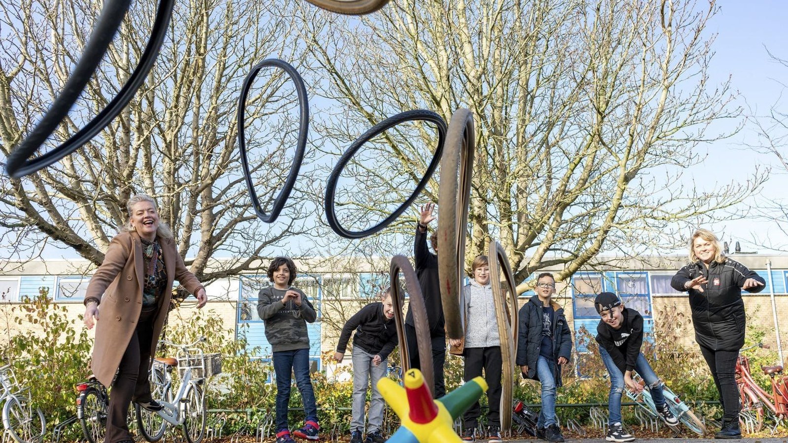 Volwassenen en kinderen spelen op sportterrein met zwarte gespannen touwen en gekleurde speeltoestellen onder kale bomen