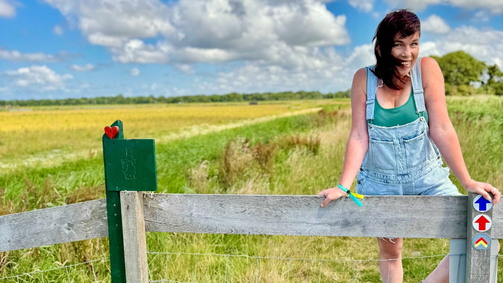 Persoon in spijkerpak leunend op hek in landschap met grasland en gele bloemen