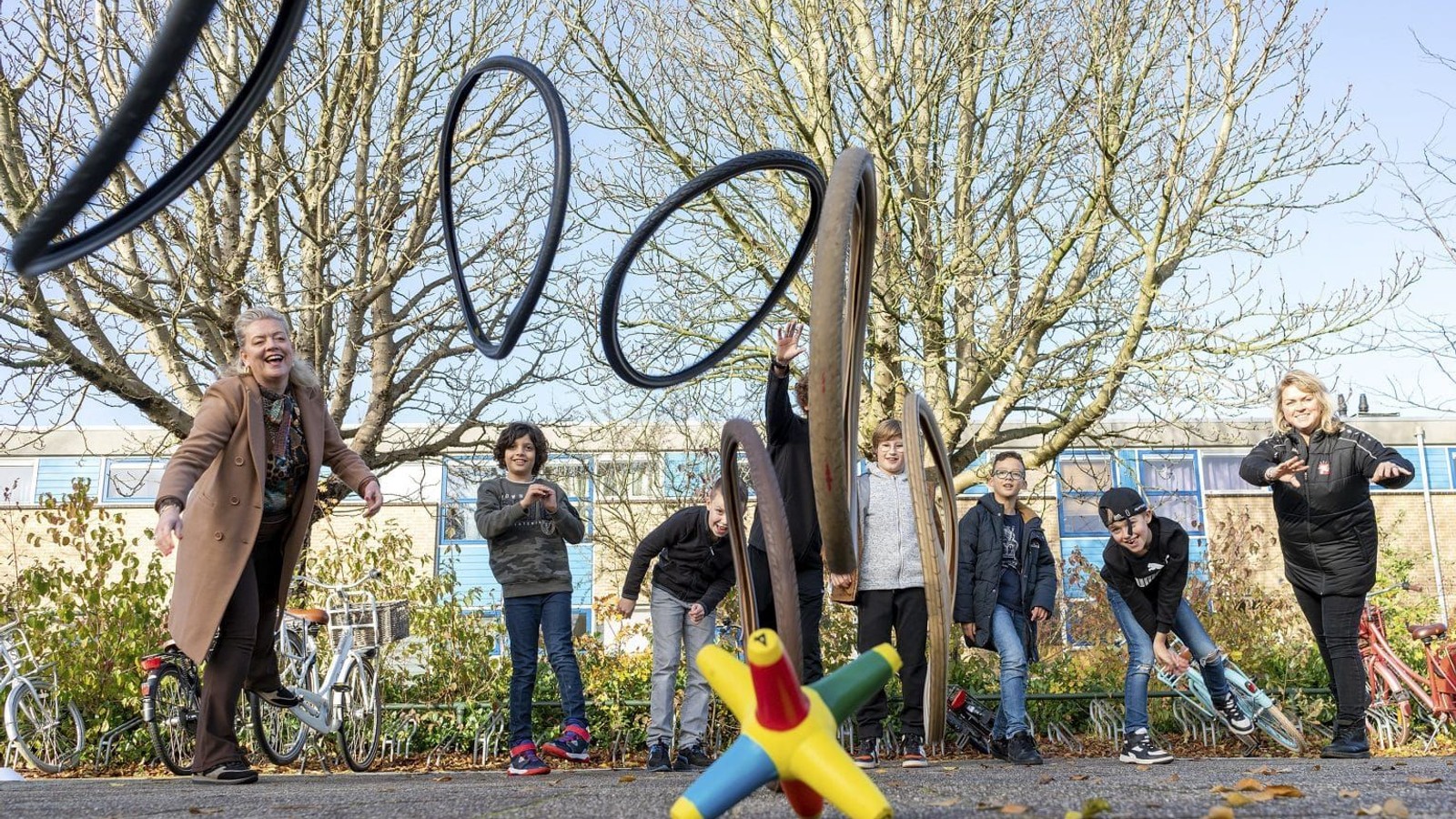 Volwassenen en kinderen spelen op sportterrein met zwarte gespannen touwen en gekleurde speeltoestellen onder kale bomen