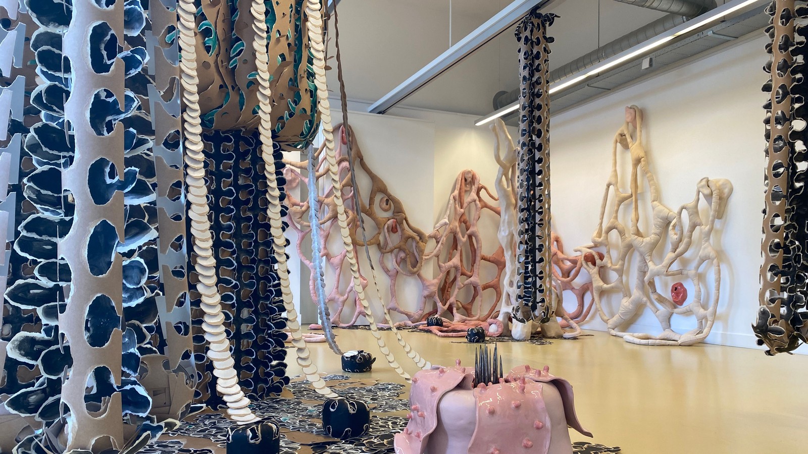 Kunstinstallatie met hangende patterned stoffen in blauw en beige, golvend papierwerk en sculpturen.