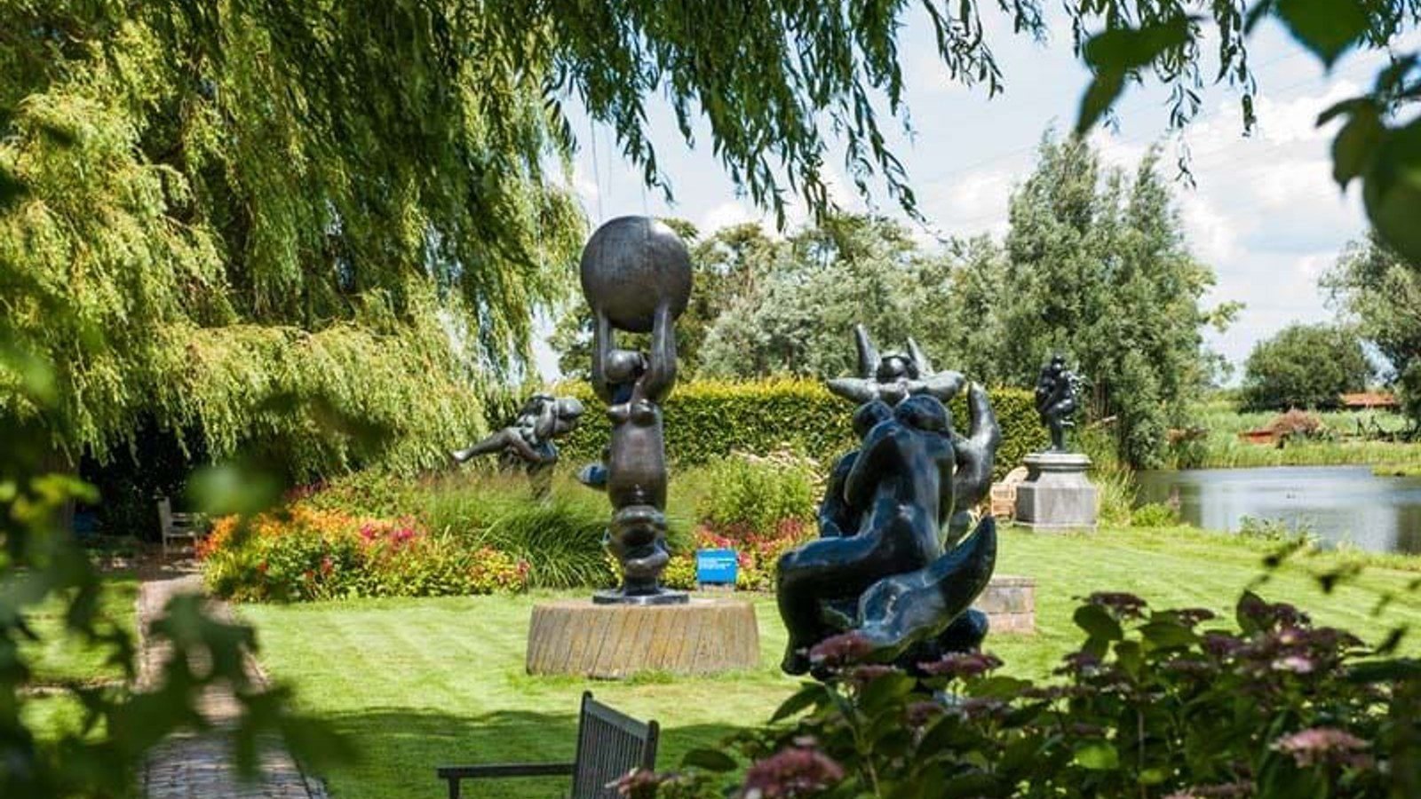 Tuinlandschap met donkere beeldhouwwerken tussen groene bomen, struiken en water