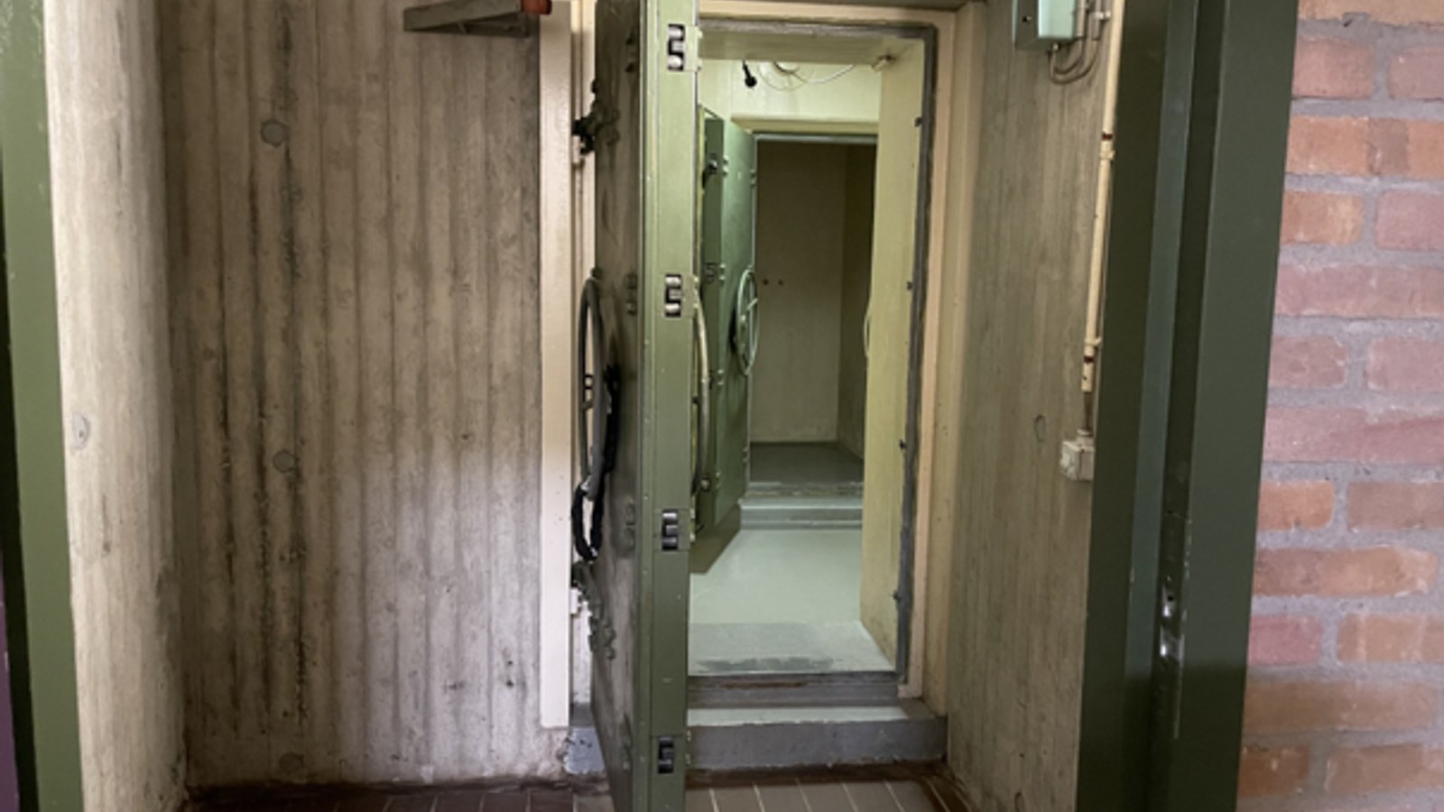 Geopende stalen deur in betonnen bunkergang met verlichte gang erachter