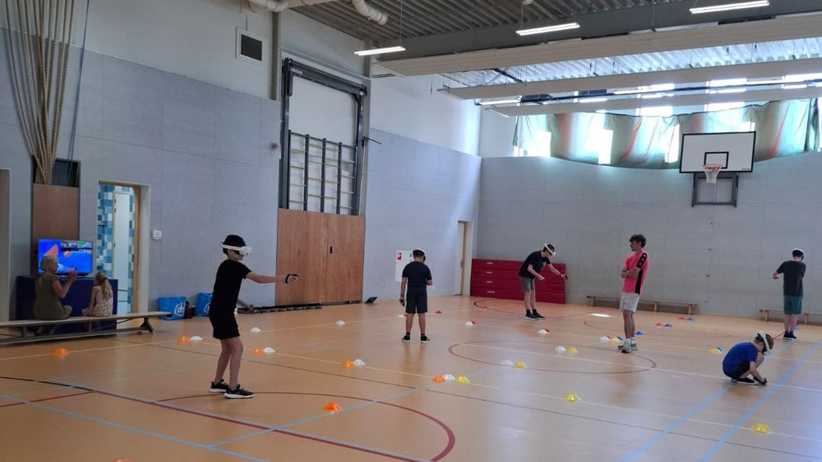 Jongeren spelen bewegingsspellen op houten sportvloer in sporthal, gekleurde pionnen verspreid