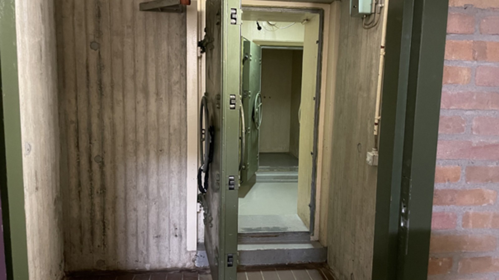 Geopende stalen deur in betonnen bunkergang met verlichte gang erachter