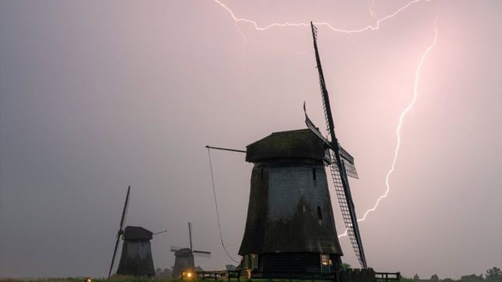 Twee molens met draaiende wieken onder een stormachtige lucht met bliksem