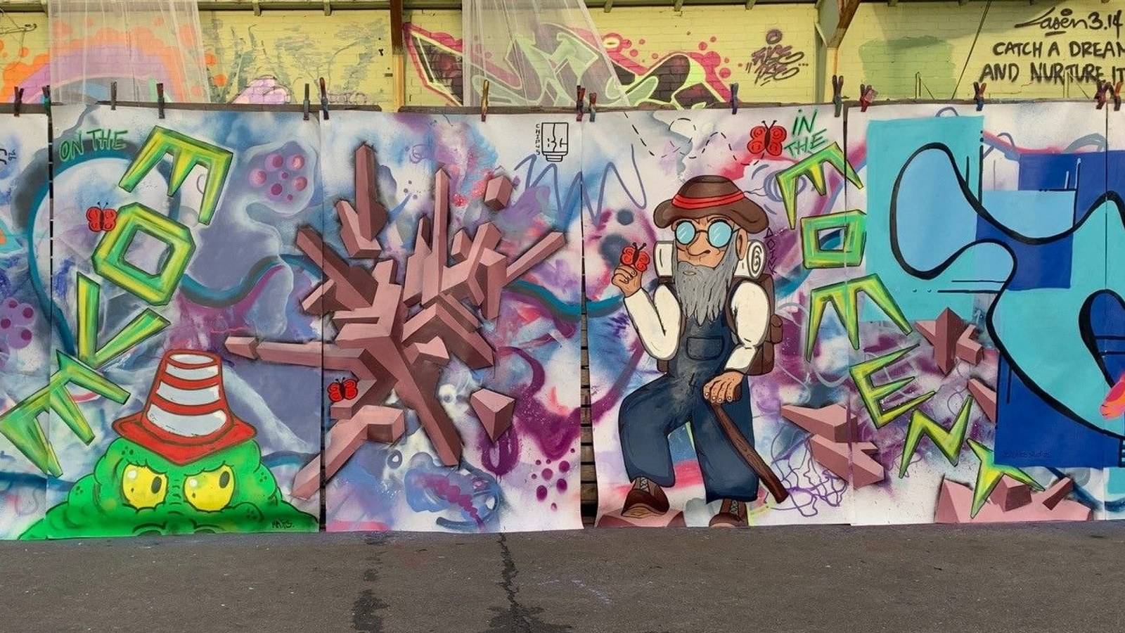 Drie kleurige muurschilderingen met abstracte vormen, personages en graffiti-stijl artwork op zijwand met diverse kleuren.