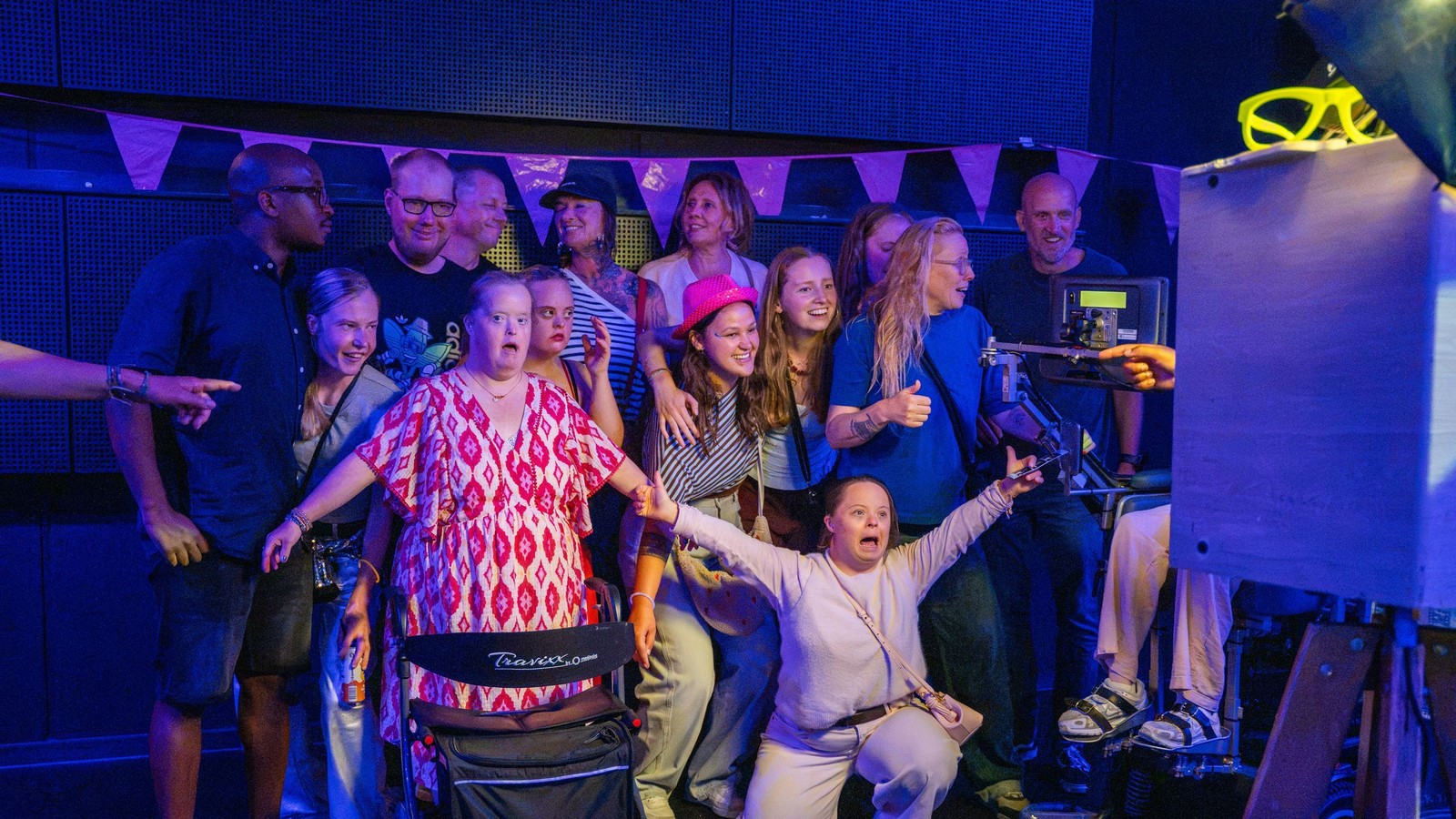 Groep mensen dansend en poseren op verlichte dansvloer met paarse en blauwe verlichting in zaal.