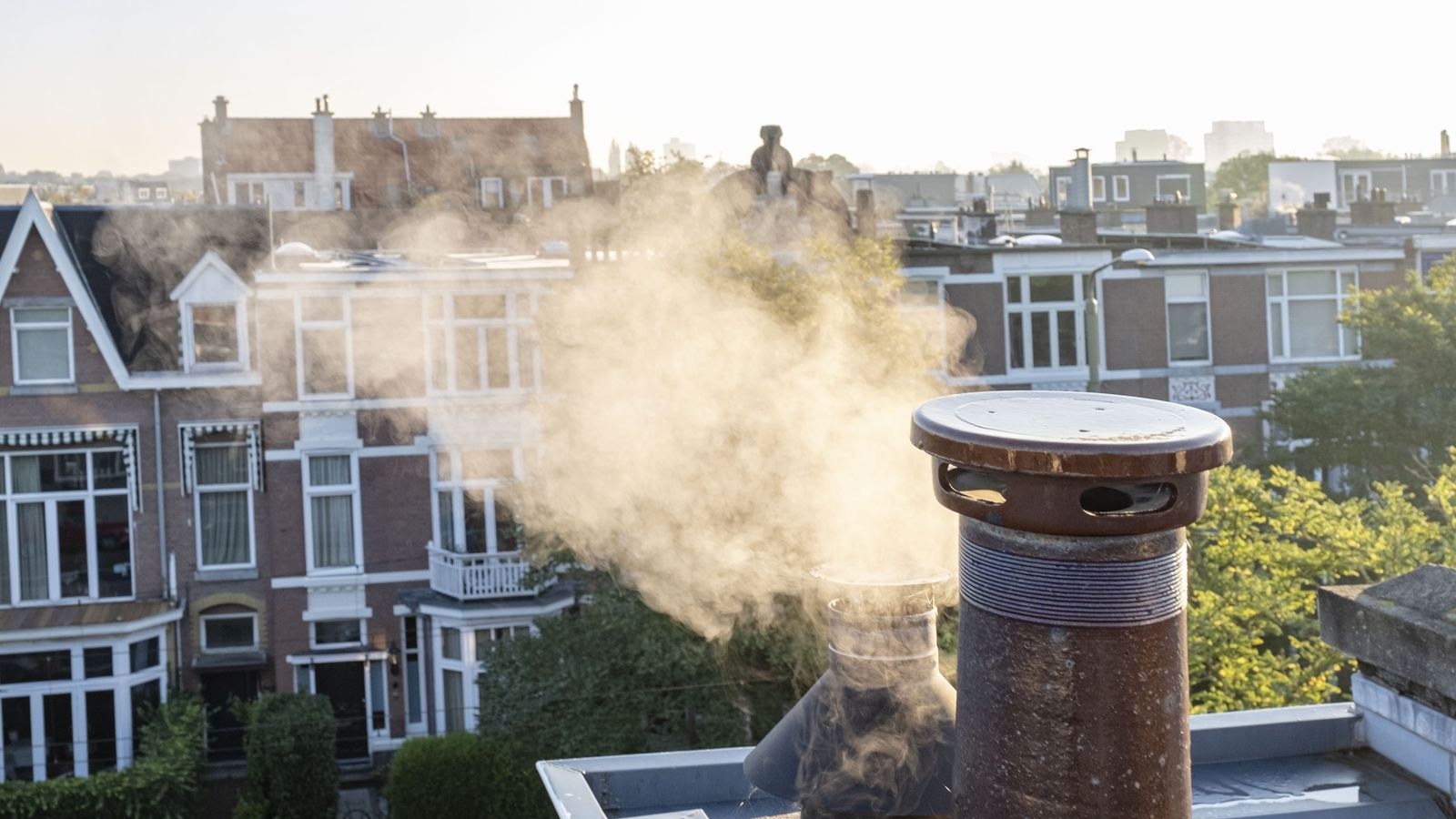 Rij woningen met daaroverheen stoom uitstotende schoorsteen, historische gebouwen op achtergrond