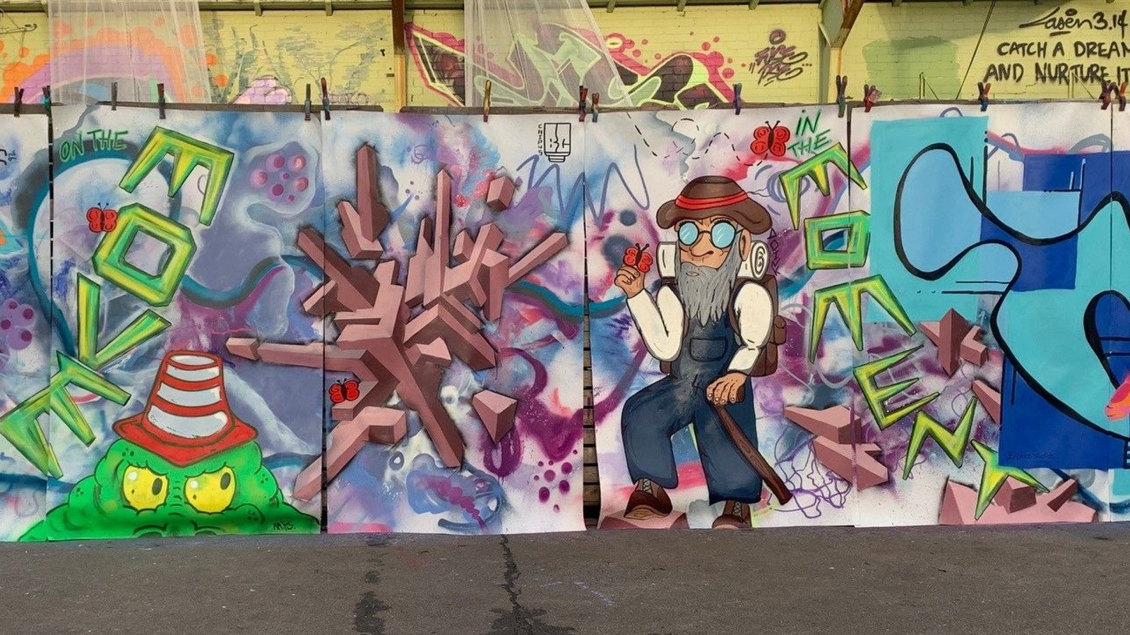 Drie kleurige muurschilderingen met abstracte designs, gestileerde personages en graffiti-art in groene, roze en blauwe tinten op wand.
