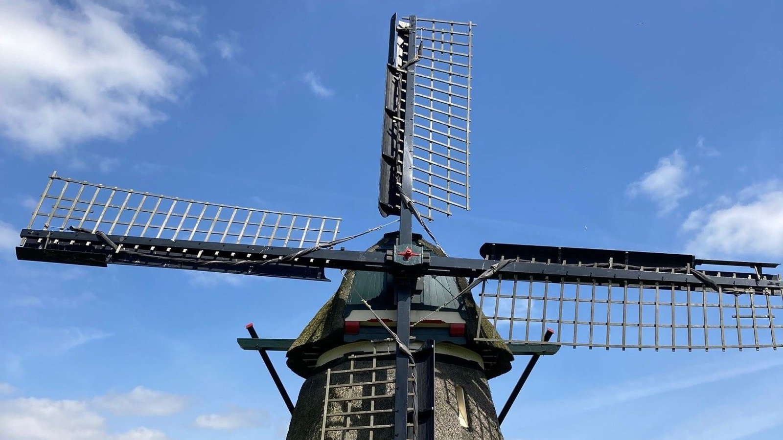 Gedeeltelijke close-up van een molen met draaiende wieken tegen blauwe lucht met wolken.