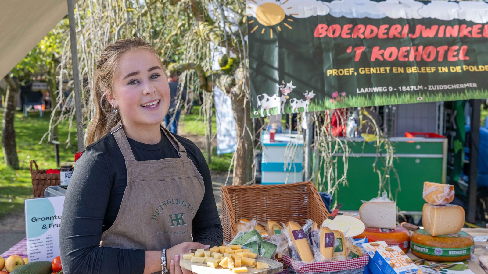 Vrouw bij marktstand met kaas en lokale producten, bord 'T Roehotel zichtbaar