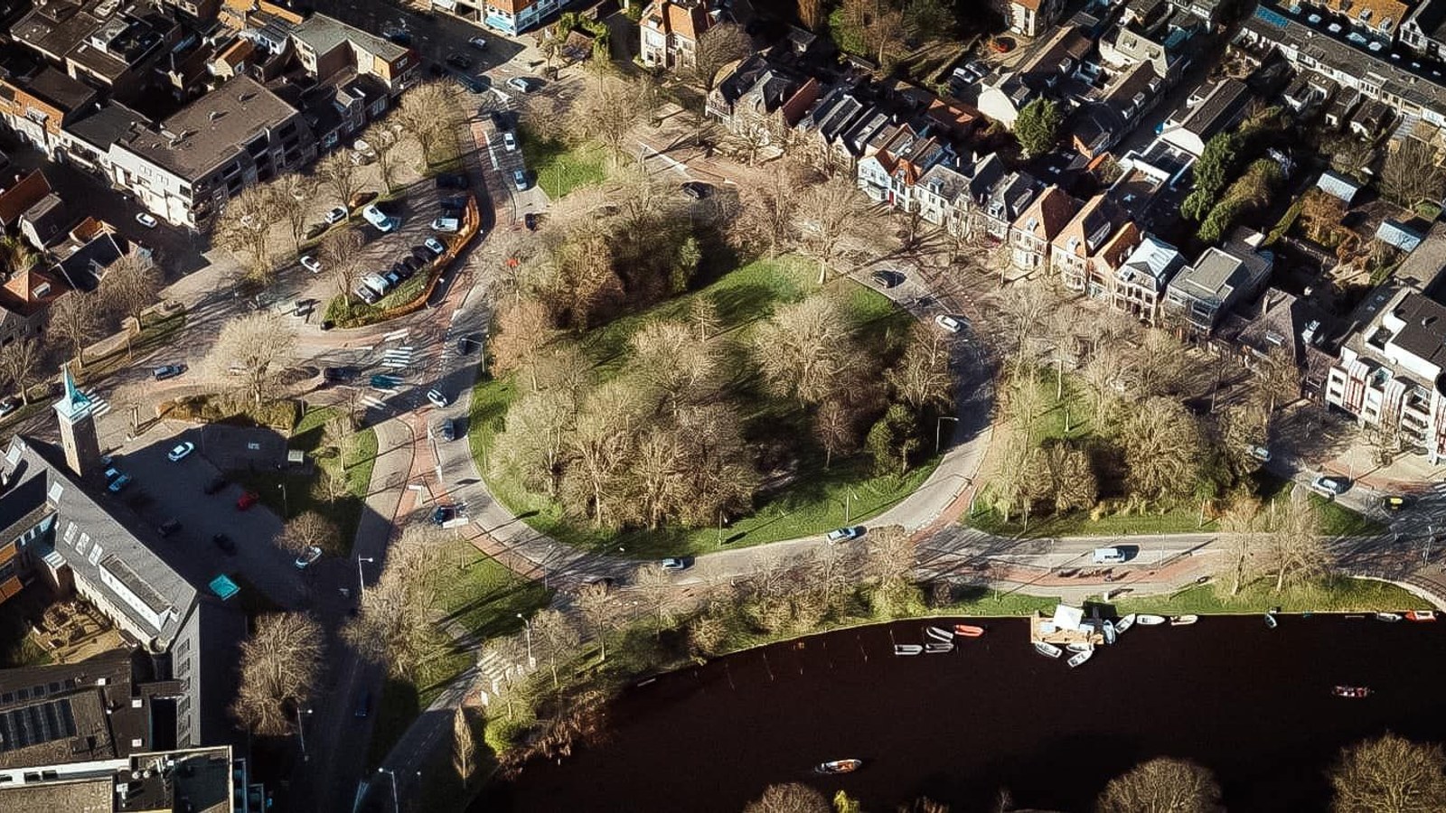 Luchtfoto van rotonde met bomen, gras, water en omringgende woongebouwen met gevels.
