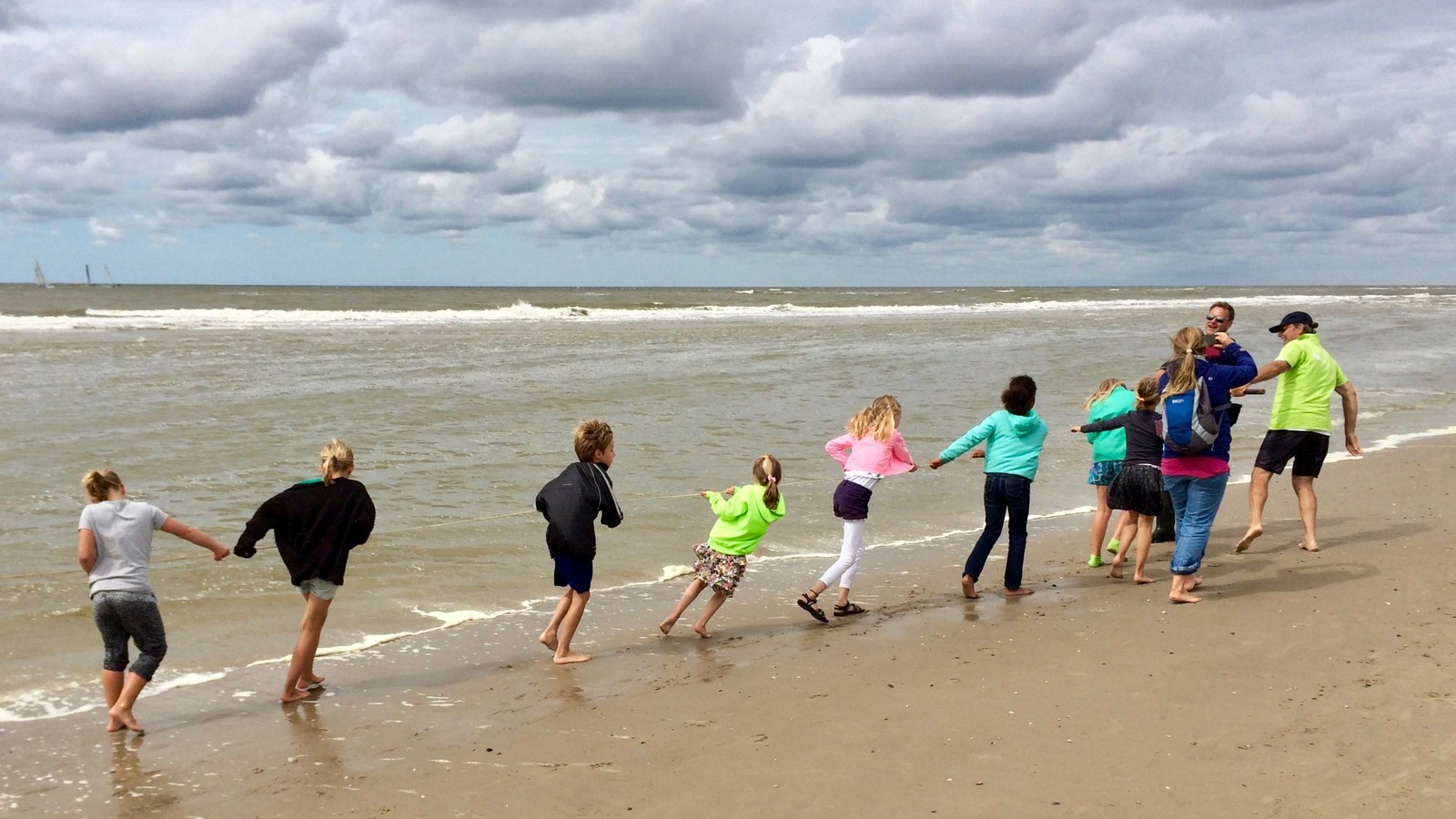 Groep kinderen loopt hand in hand het water in op een zandstrand met golven