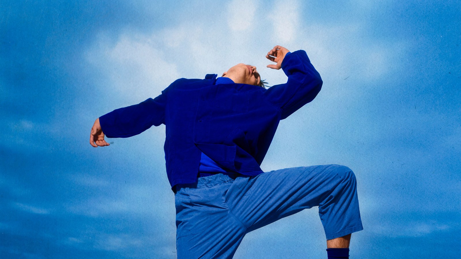 Theaterbeeld bij De lente vatte vlam: persoon in blauwe kleding met opgeheven knie tegen een blauwe lucht.